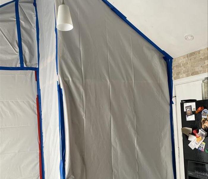 Kitchen with a white plastic tarp hanging from the ceiling extending to the floor. Blue tape secures the tarp.